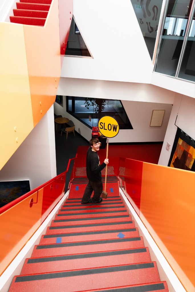 Portrait on red stairs holding the yellow SLOW road sign