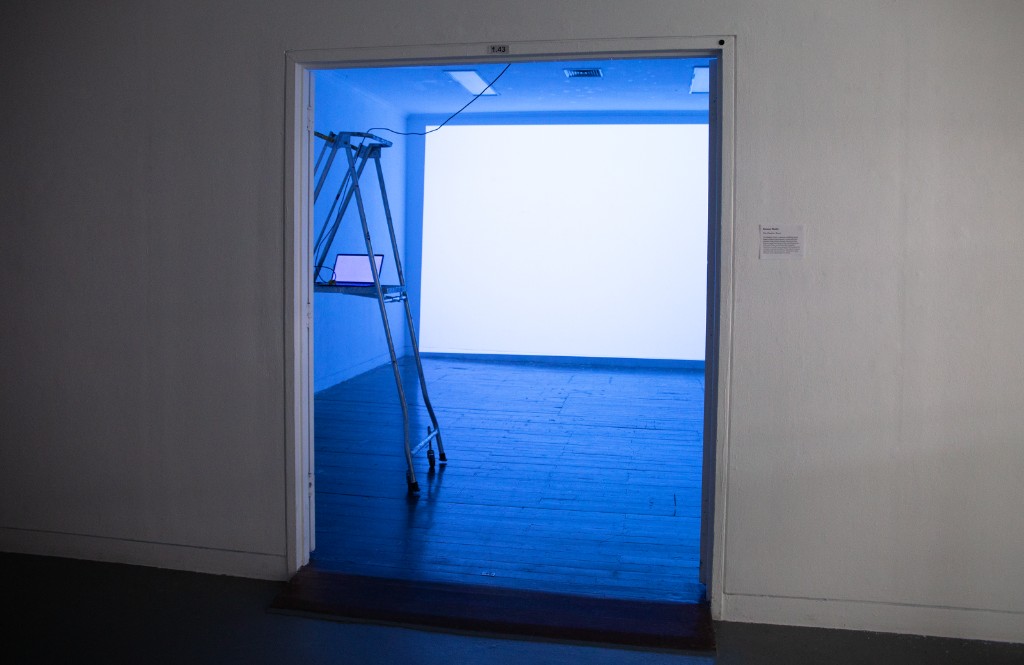 The Weather Room — view through a doorway into the installation, blue-lit space with equipment and ladder